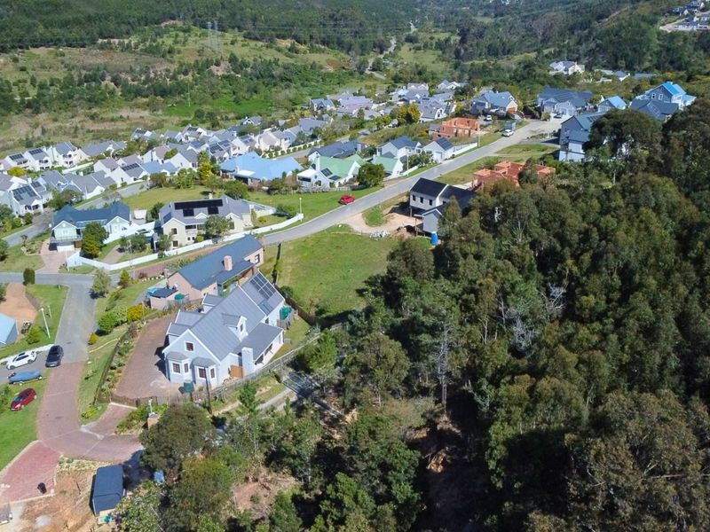 An aerial view of a residential estate featuring established homes, paved streets, and surrounding natural woodland landscape.