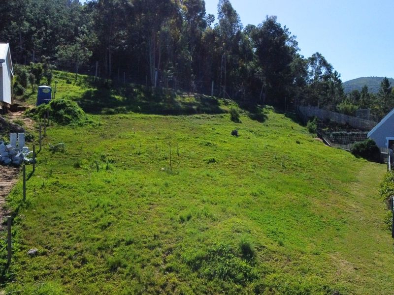 An aerial view of a sloped residential vacant land plot featuring surrounding trees and adjacent residential structures.
