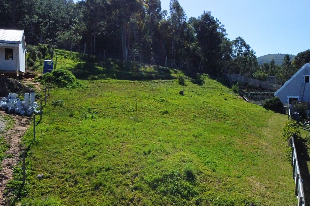 An aerial view of a sloped residential vacant land plot featuring surrounding trees and adjacent residential structures.