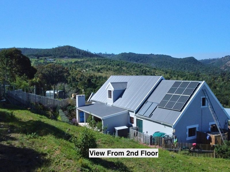 Aerial view of a residential property featuring a metal roof with integrated solar panels, set against a scenic mountainous landscape.