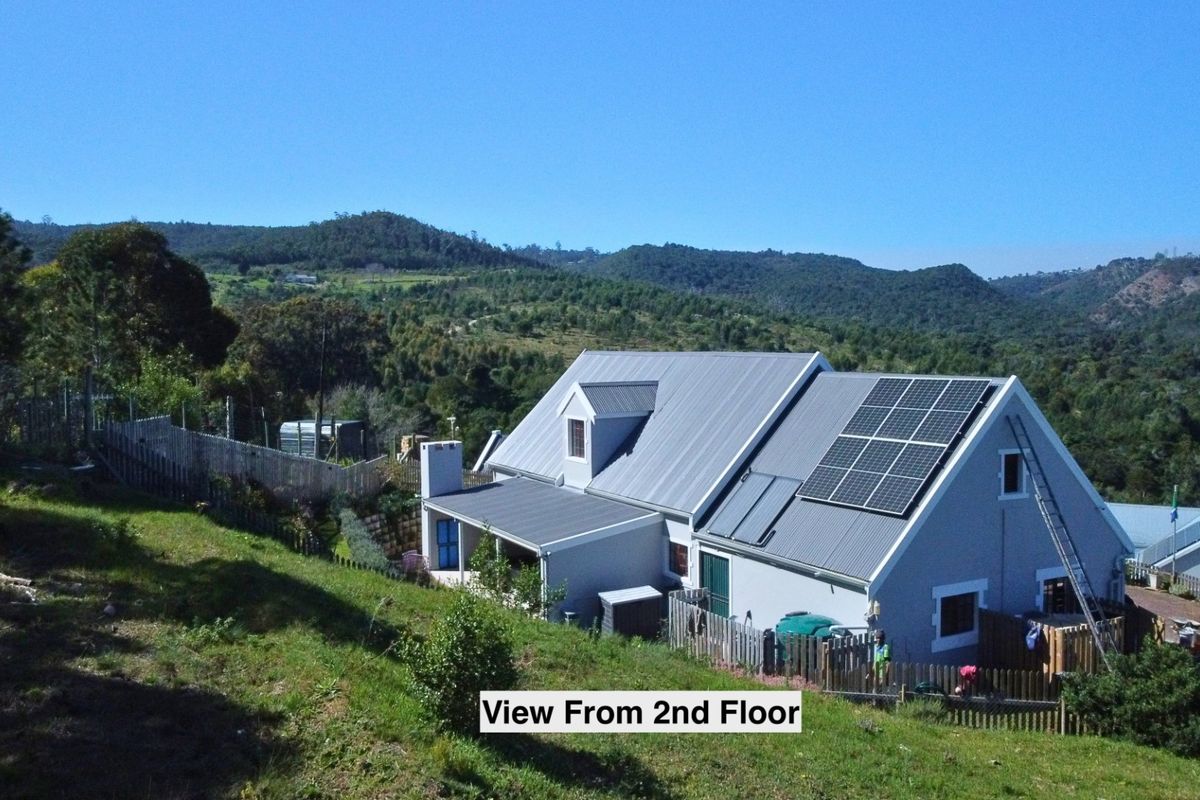 Aerial view of a residential property featuring a metal roof with integrated solar panels, set against a scenic mountainous landscape.