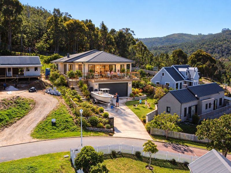 Aerial view of a residential property featuring a modern home with a raised deck, landscaped garden, and concrete driveway in a scenic estate setting.