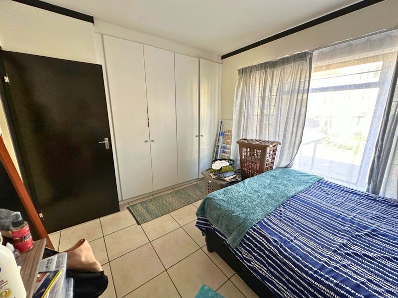 A bedroom featuring built-in cupboards, tiled flooring, and a large window allowing natural light.