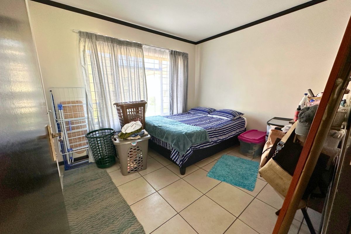 A functional bedroom featuring tiled flooring, security bars on the window, and neutral wall finishes, offering a practical space for rest.