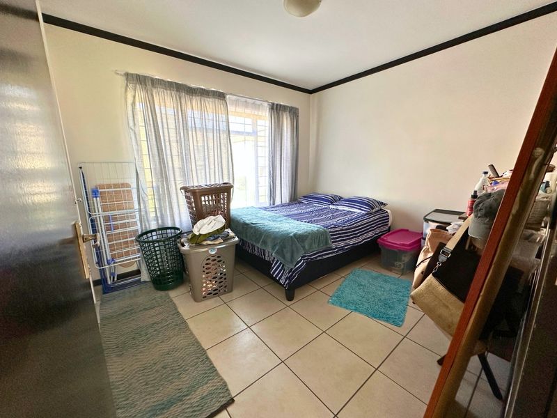 A functional bedroom featuring tiled flooring, security bars on the window, and neutral wall finishes, offering a practical space for rest.