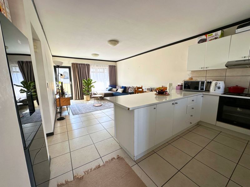 Open-plan living area featuring a functional kitchen with a central island, tiled flooring, and direct access to an outdoor space through a sliding door.