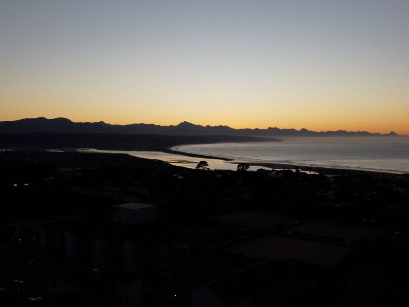 A scenic aerial view of the coastline and mountain range at sunset, showcasing the natural landscape surrounding the property.
