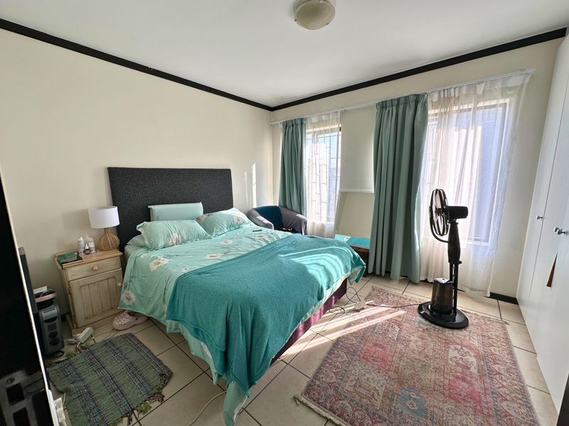 A bedroom featuring tiled flooring, built-in cupboards, and dual windows with curtains, providing natural light and functional storage space.