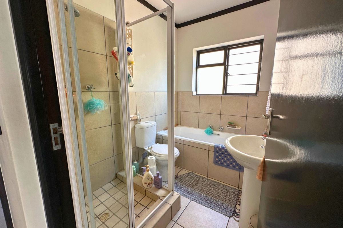 A functional bathroom featuring a shower enclosure, bathtub, pedestal basin, and toilet with neutral wall and floor tiling.