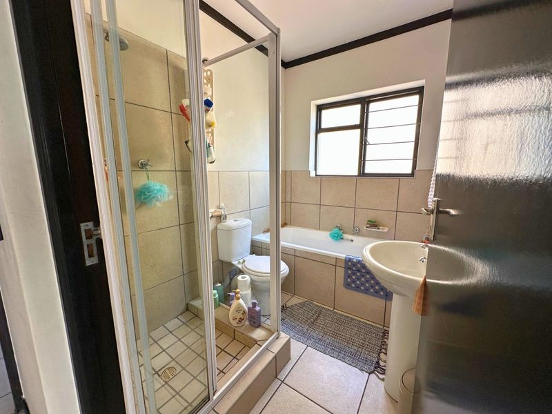 A functional bathroom featuring a shower enclosure, bathtub, pedestal basin, and toilet with neutral wall and floor tiling.