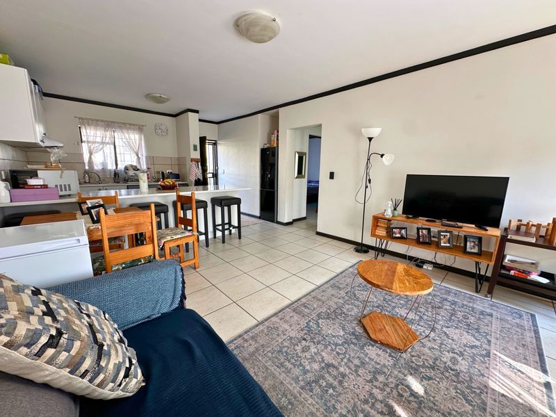 Open-plan living and kitchen area featuring tiled flooring, a breakfast bar island, and functional kitchen cabinetry.