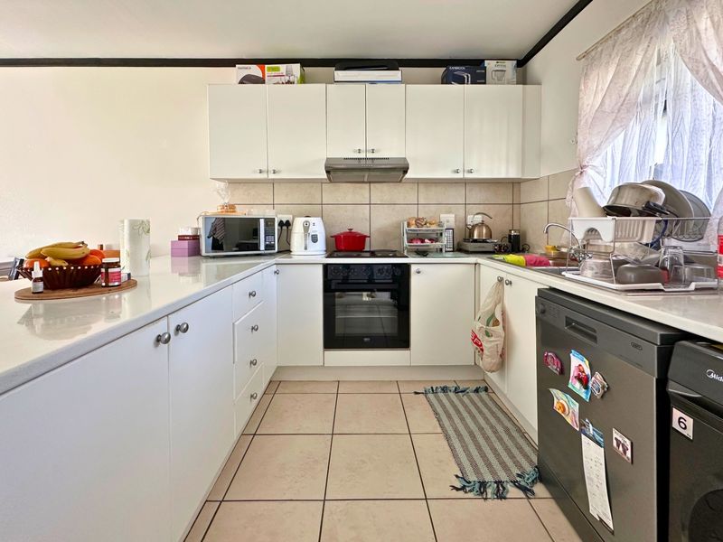 A functional U-shaped kitchen featuring white cabinetry, tiled splashbacks, built-in oven and hob, and tiled flooring.