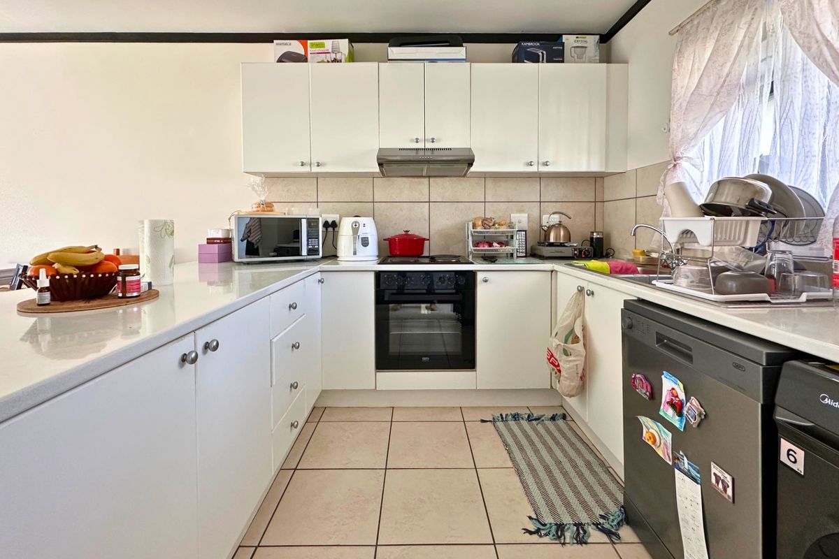 A functional U-shaped kitchen featuring white cabinetry, tiled splashbacks, built-in oven and hob, and tiled flooring.
