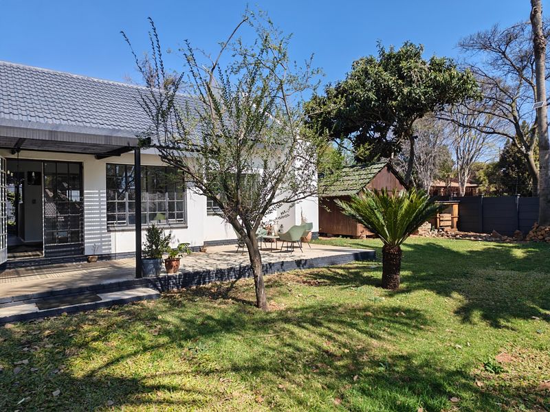 Rear view of the house featuring a covered patio, well-maintained garden, and a small wooden storage shed.