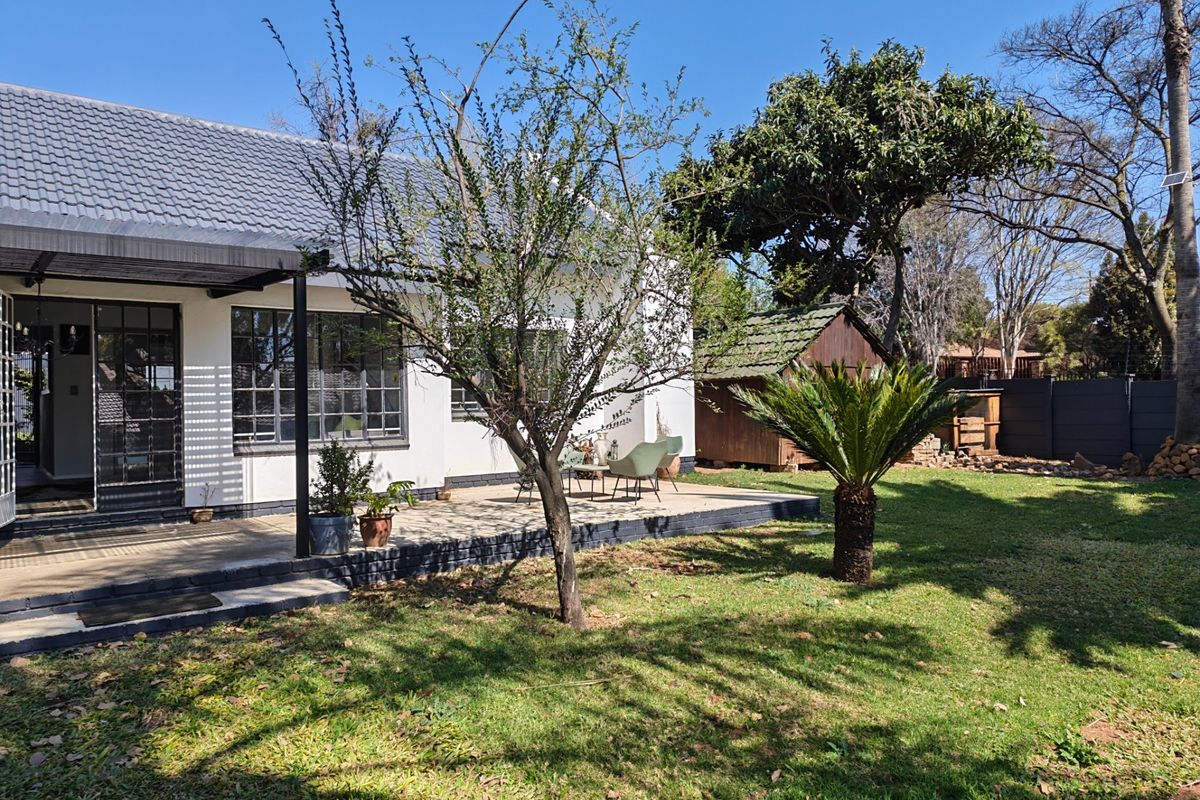 Rear view of the house featuring a covered patio, well-maintained garden, and a small wooden storage shed.