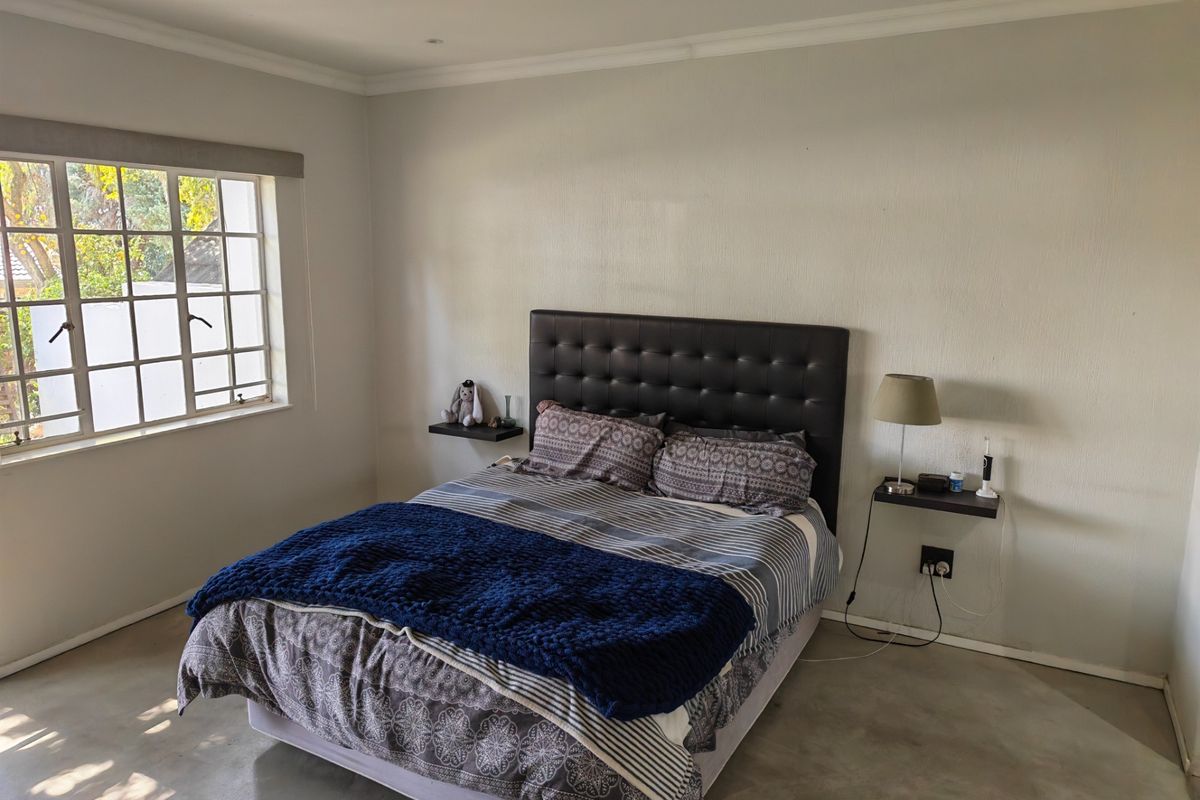 A well-lit bedroom featuring polished concrete floors, recessed ceiling lighting, and convenient floating bedside shelves.