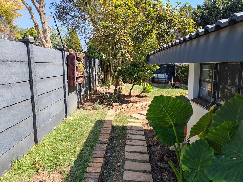 A well-maintained side garden featuring a brick paved pathway, mature trees, and a secure boundary wall with electric fencing.