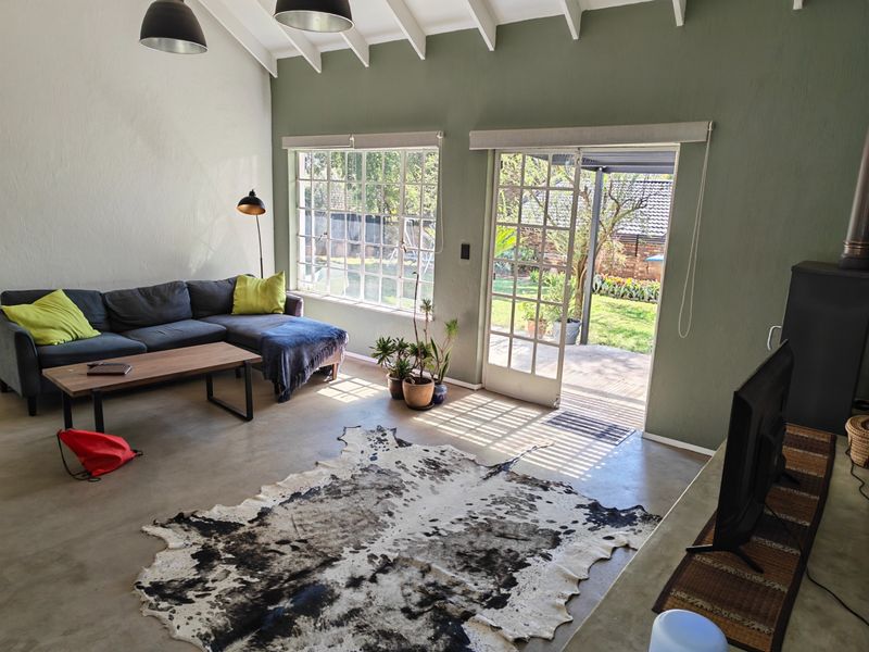 Spacious living room featuring exposed rafters, polished concrete floors, and large windows with direct access to the rear garden through french doors.