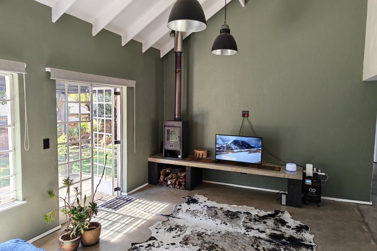 Spacious living room featuring a vaulted ceiling with exposed rafters, concrete flooring, a wood-burning fireplace, and direct access to the garden through french doors.
