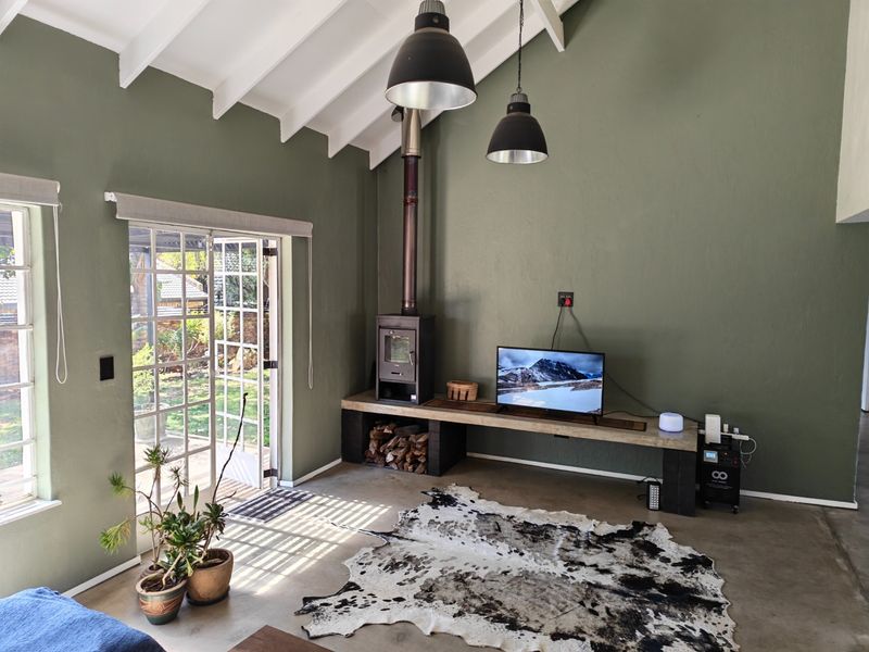 Spacious living room featuring a vaulted ceiling with exposed rafters, concrete flooring, a wood-burning fireplace, and direct access to the garden through french doors.
