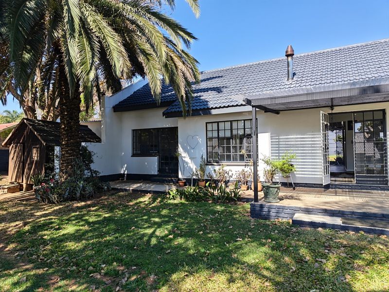 Rear view of the house featuring a tiled roof, steel-framed windows, and a covered patio area overlooking the garden.