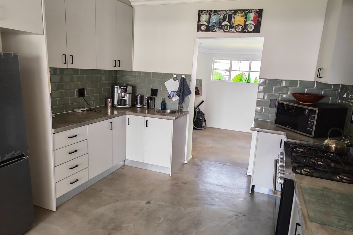 Modern kitchen featuring white cabinetry, subway tile backsplash, gas cooktop, and polished concrete flooring, leading into an adjacent utility space.