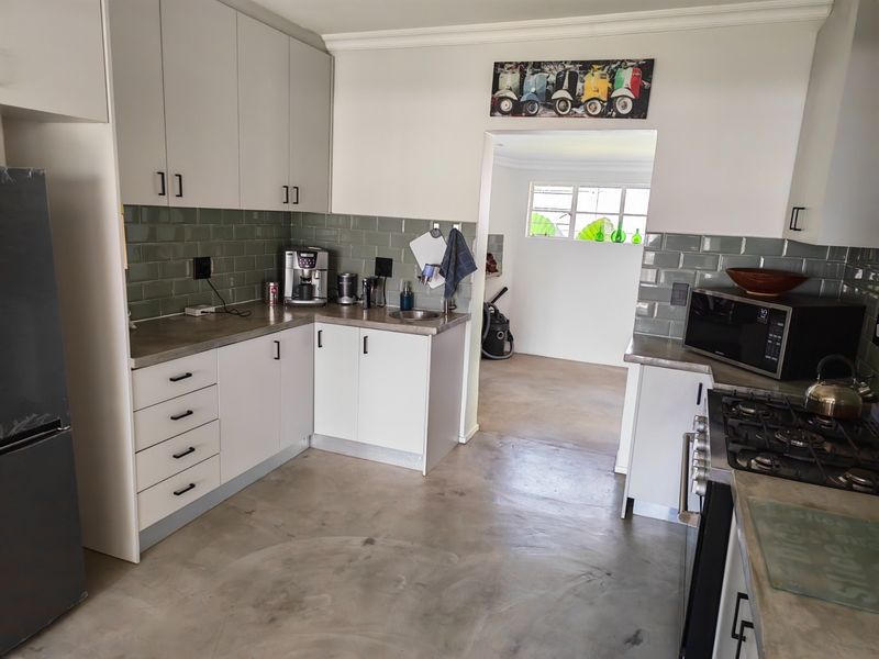 Modern kitchen featuring white cabinetry, subway tile backsplash, gas cooktop, and polished concrete flooring, leading into an adjacent utility space.