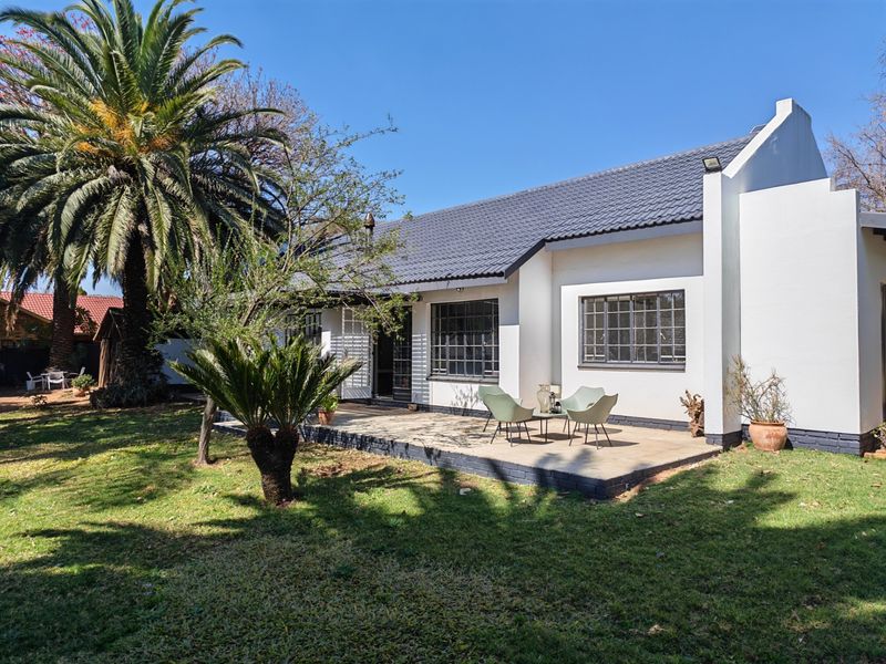 Rear view of the house featuring a tiled roof, concrete patio area, and established garden surroundings.