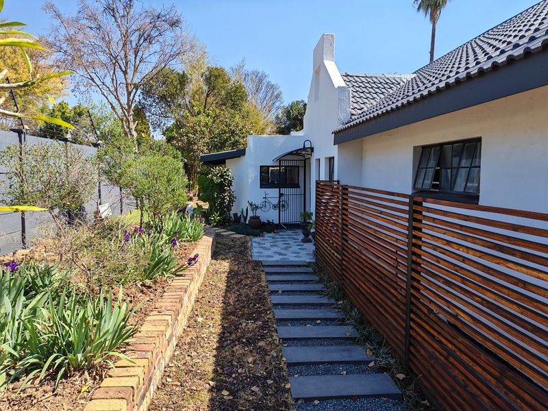 A well-maintained rear exterior featuring a stone paver walkway, timber privacy screening, and a landscaped garden with a brick retaining wall.