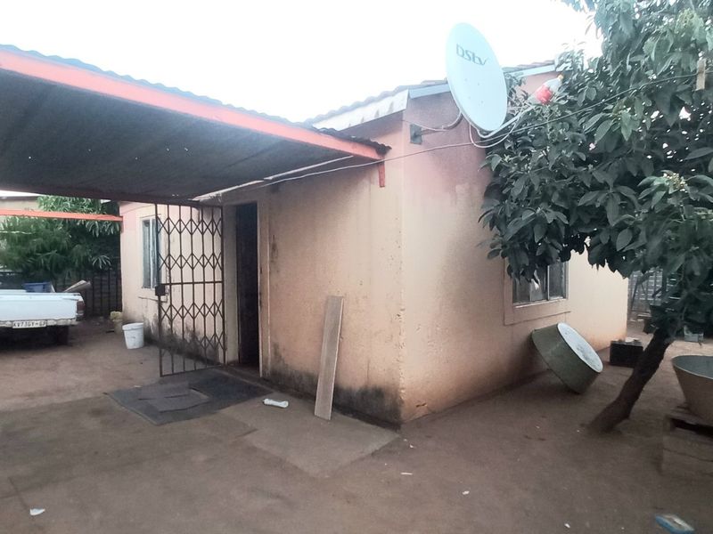 Rear exterior view of the property featuring a metal carport structure, security gate, and satellite dish installation.