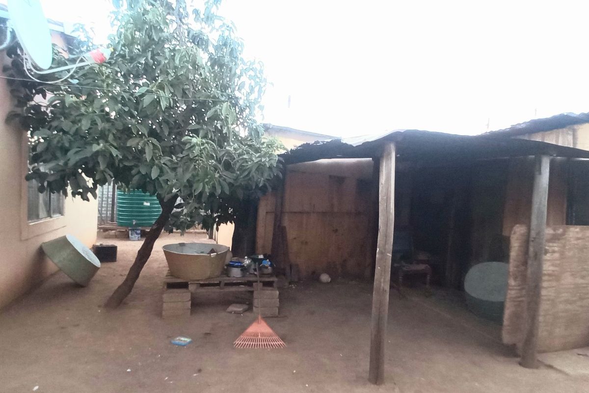 Rear exterior area featuring a basic covered structure with timber supports, a satellite dish, and a water tank in a weathered condition.