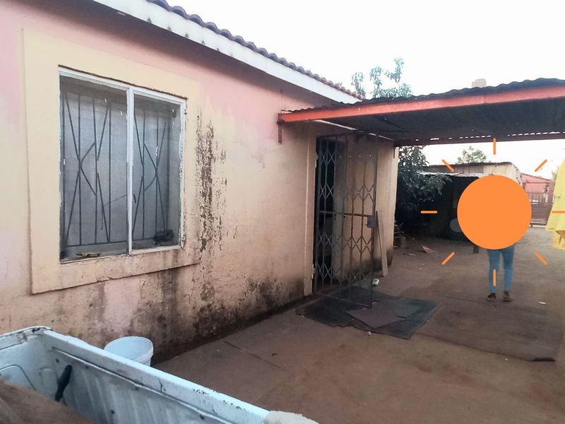 Rear exterior view of the property featuring a covered patio area, security gates, and significant wear to the exterior wall finishes.