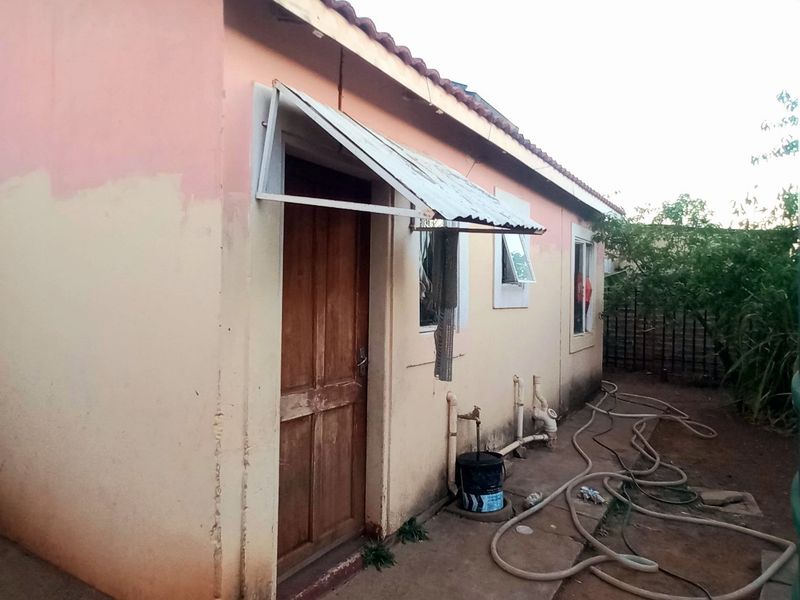 Rear exterior view of the house showing a tiled roof, metal awning over the entrance, and external plumbing fixtures.