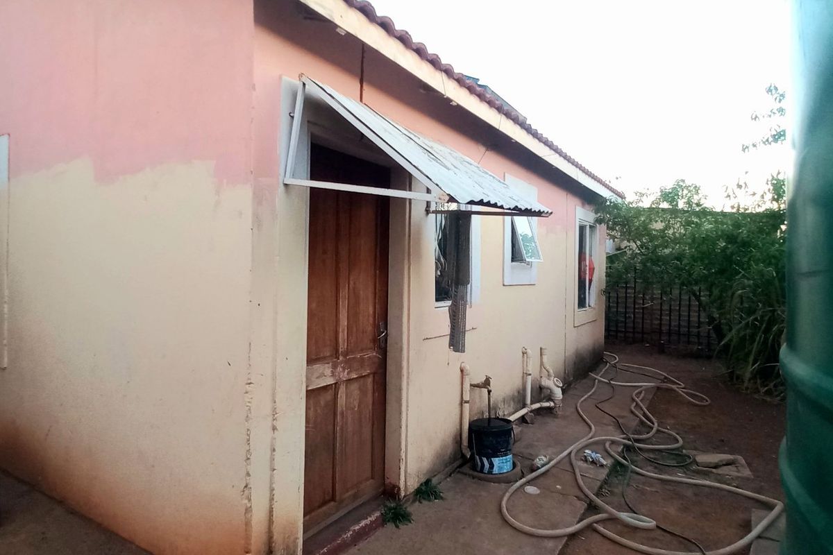 Rear exterior view of the house showing a tiled roof, metal awning over the entrance, and external plumbing fixtures.