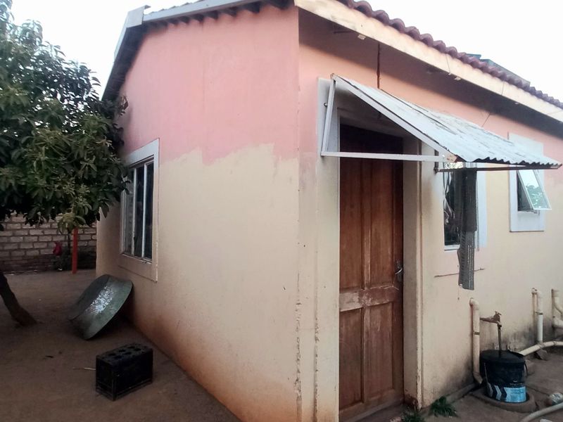 Rear exterior view of a single-story house featuring a tiled roof, timber door with a metal awning, and visible exterior plumbing.
