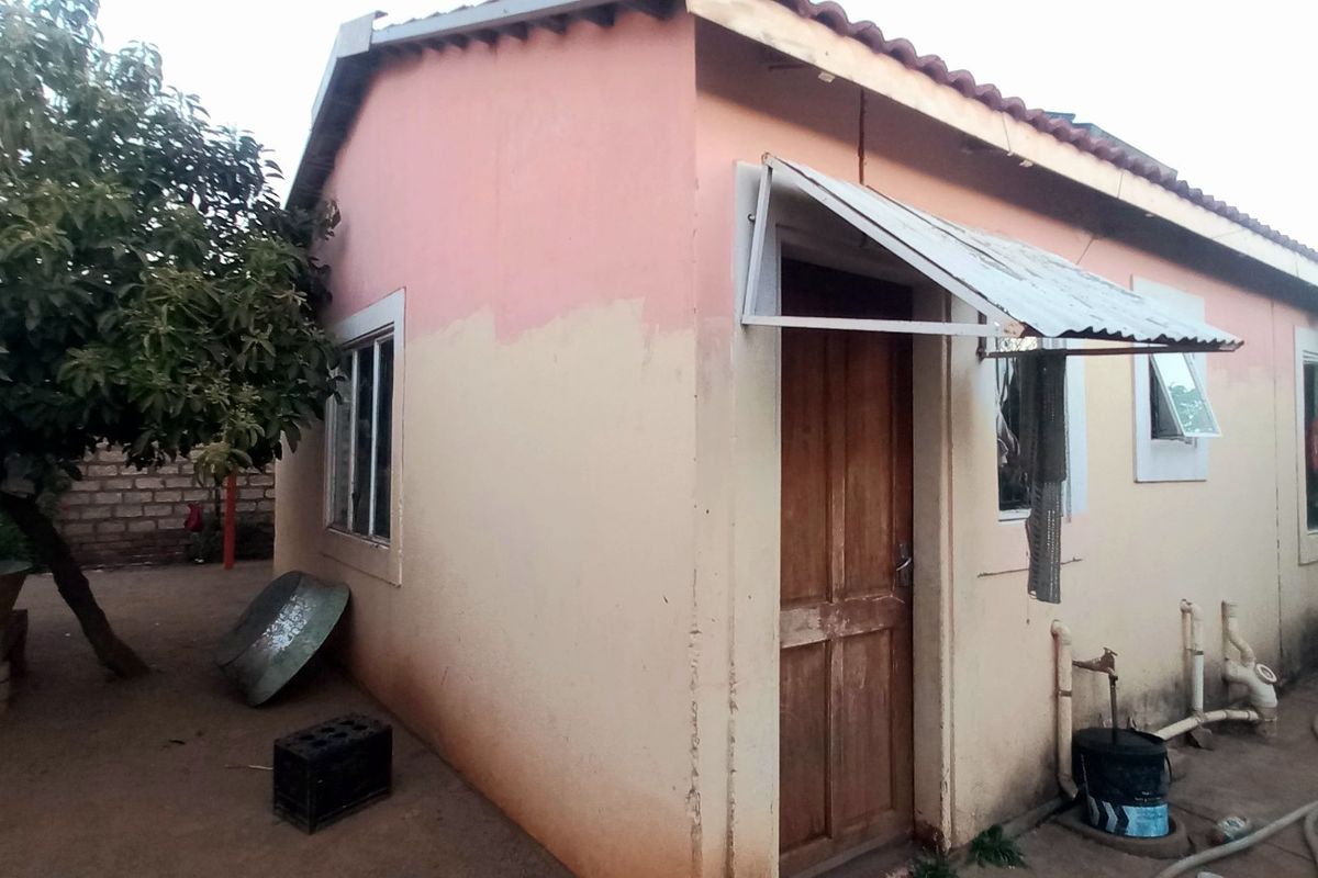 Rear exterior view of a single-story house featuring a tiled roof, timber door with a metal awning, and visible exterior plumbing.