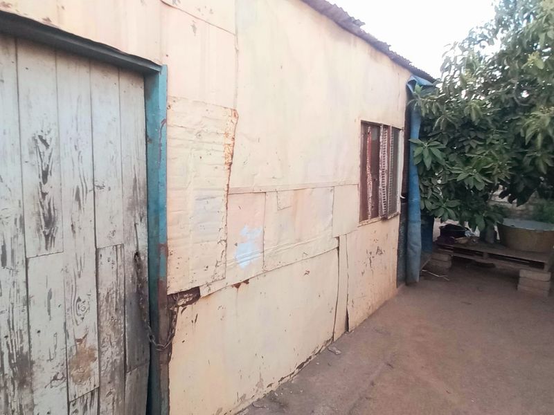 Exterior view of a structure featuring corrugated metal wall cladding and a weathered timber door in a garden setting.