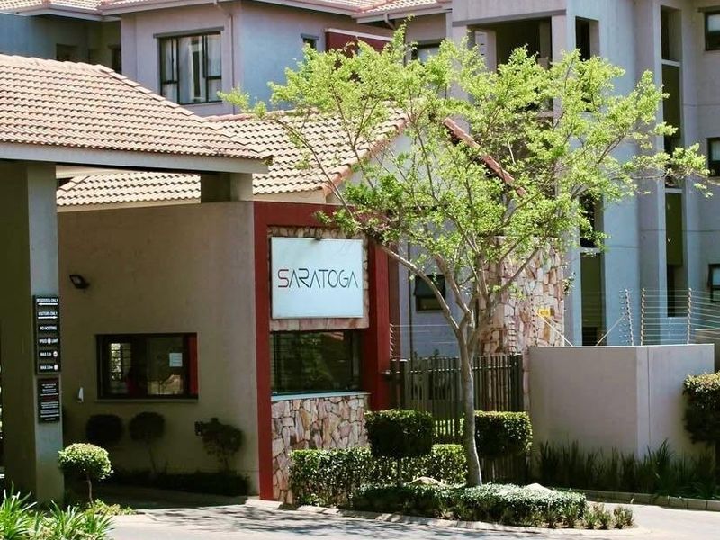 Front entrance view of the Saratoga apartment complex, featuring a secure gated access point, stone-clad pillars, and well-maintained landscaping.