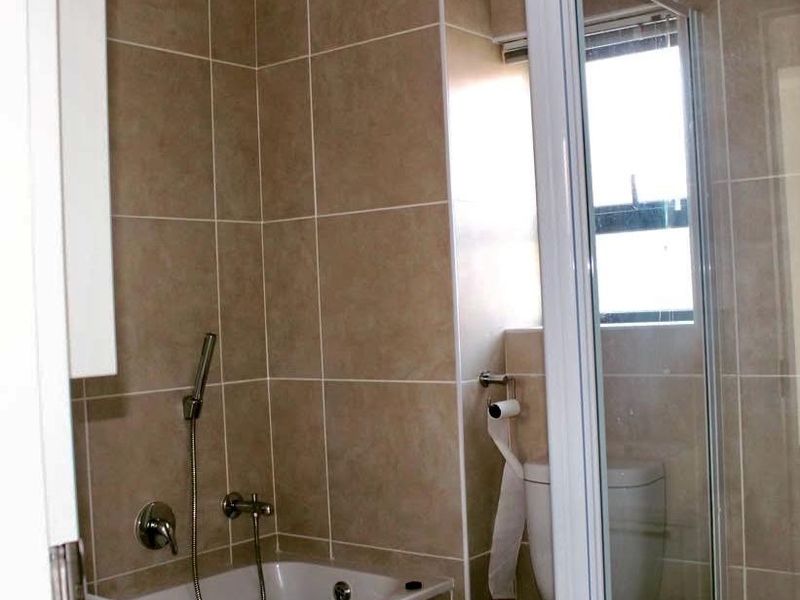 A functional bathroom featuring a built-in bathtub with a handheld shower mixer, a toilet, and neutral wall tiling.