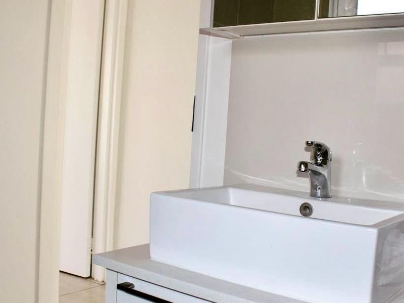 A clean, modern bathroom vanity featuring a white vessel sink, chrome mixer tap, stone countertop, and a mirrored medicine cabinet.