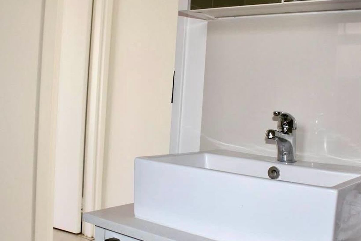 A clean, modern bathroom vanity featuring a white vessel sink, chrome mixer tap, stone countertop, and a mirrored medicine cabinet.