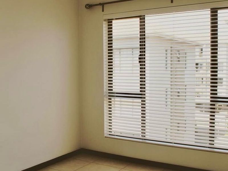 A bright, empty bedroom featuring neutral tiled flooring and fitted venetian blinds, offering a clean and versatile space ready for personalization.