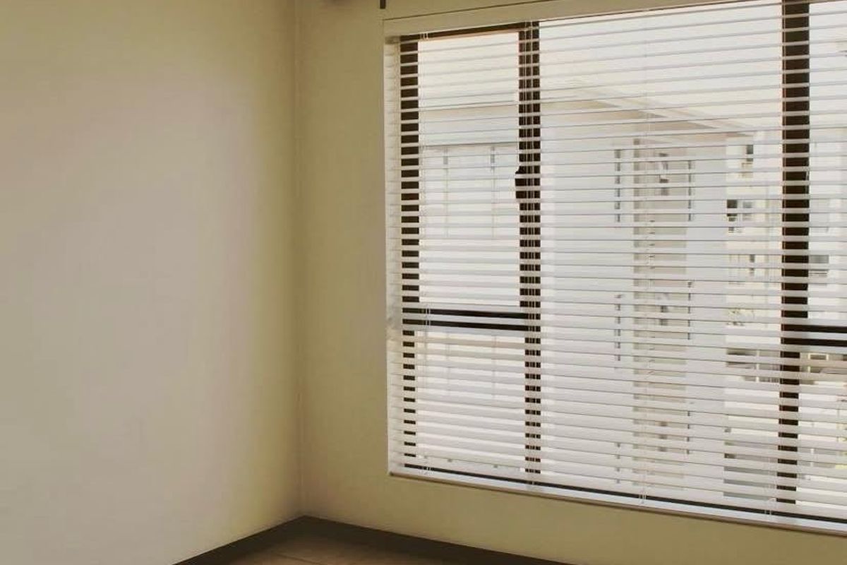 A bright, empty bedroom featuring neutral tiled flooring and fitted venetian blinds, offering a clean and versatile space ready for personalization.