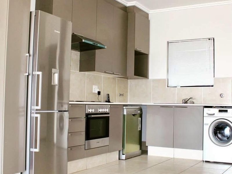 Modern kitchen featuring sleek taupe cabinetry, tiled backsplash, integrated oven and hob, and tiled flooring with ample space for appliances.