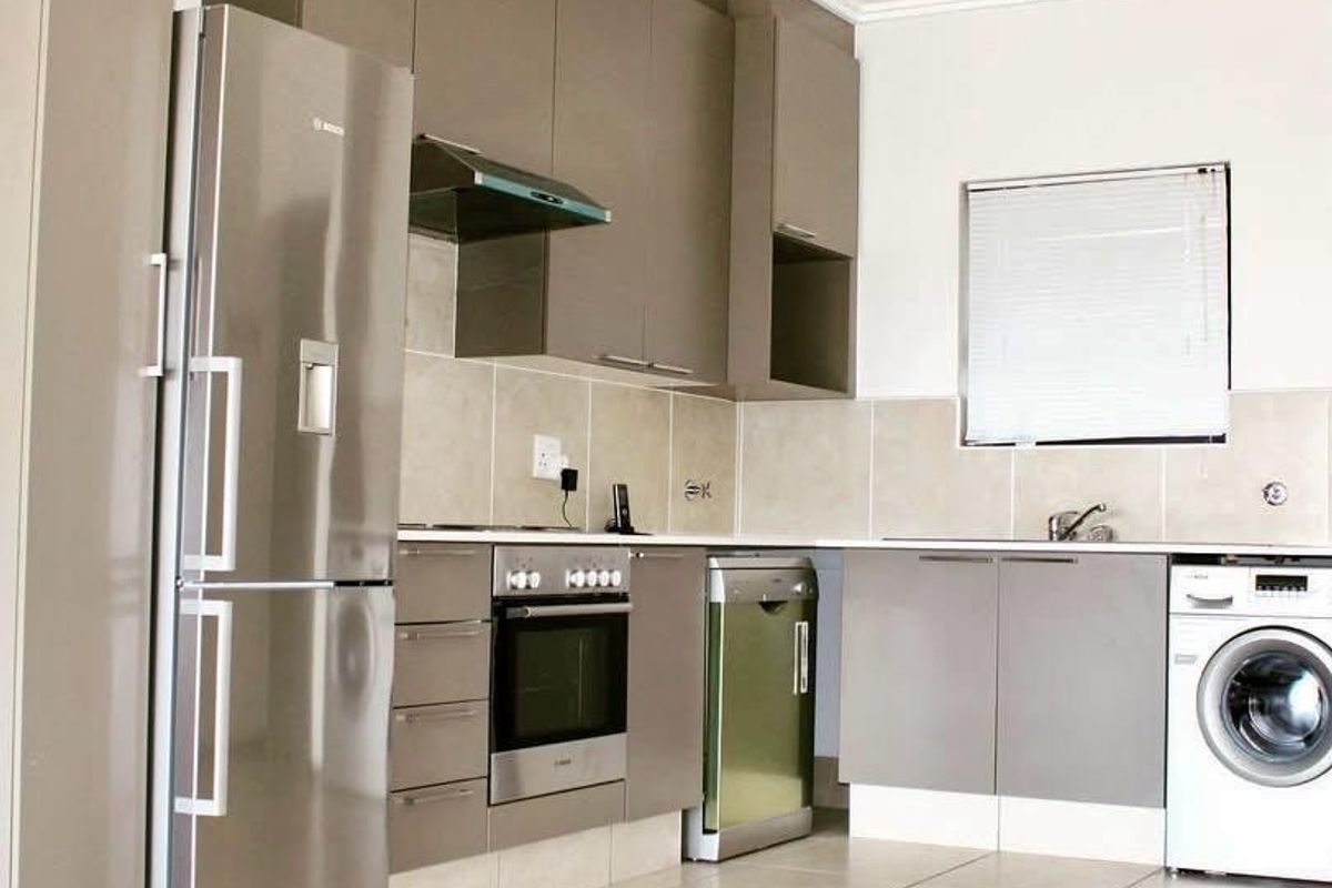 Modern kitchen featuring sleek taupe cabinetry, tiled backsplash, integrated oven and hob, and tiled flooring with ample space for appliances.