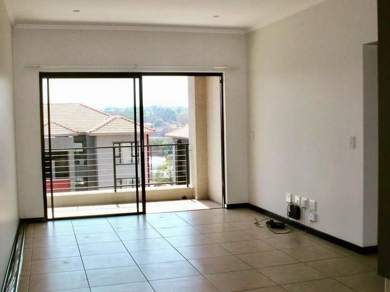 An empty, open-plan living area featuring neutral tiled flooring, recessed lighting, and a large sliding glass door leading to a private balcony.