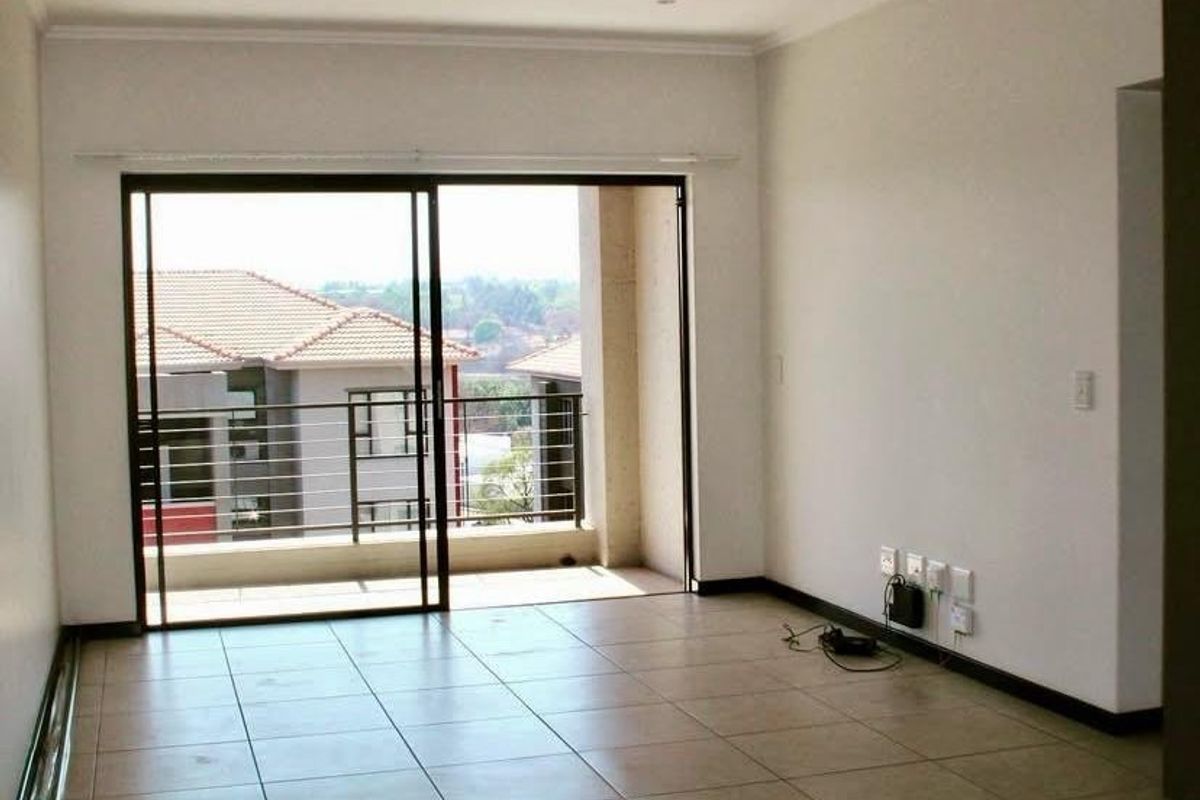 An empty, open-plan living area featuring neutral tiled flooring, recessed lighting, and a large sliding glass door leading to a private balcony.