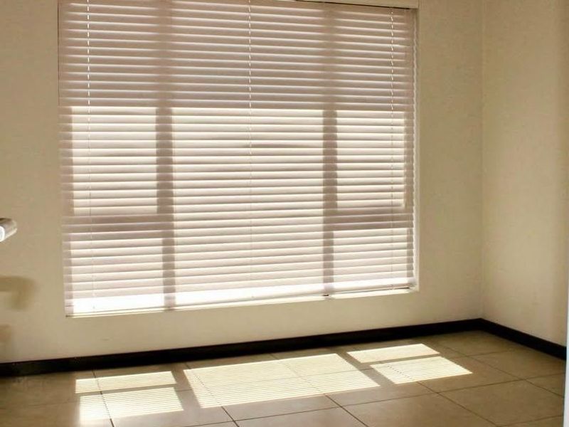 A bright, empty bedroom featuring neutral tiled flooring and fitted venetian blinds, offering a clean and versatile space ready for personalization.