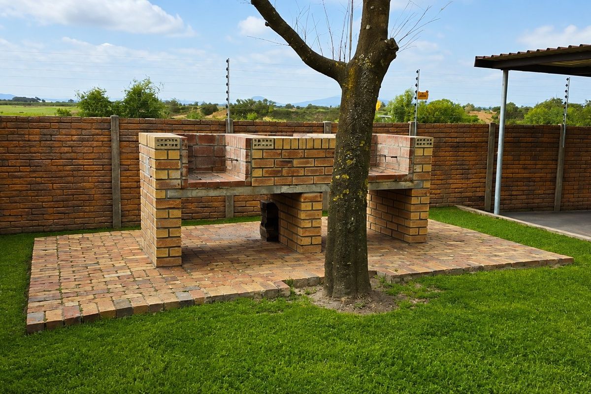 Outdoor communal area featuring a brick built-in braai, paved patio, and secure boundary wall with electric fencing.