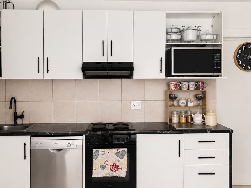 A functional kitchen featuring white cabinetry, dark countertops, a tiled splashback, and integrated appliances including an oven, hob, and dishwasher.